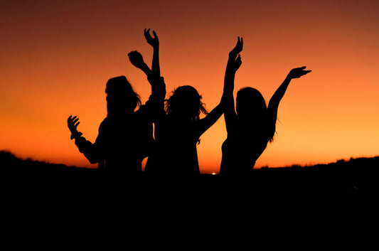 Silhouettes of three people raising their arms against an orange sunset sky.